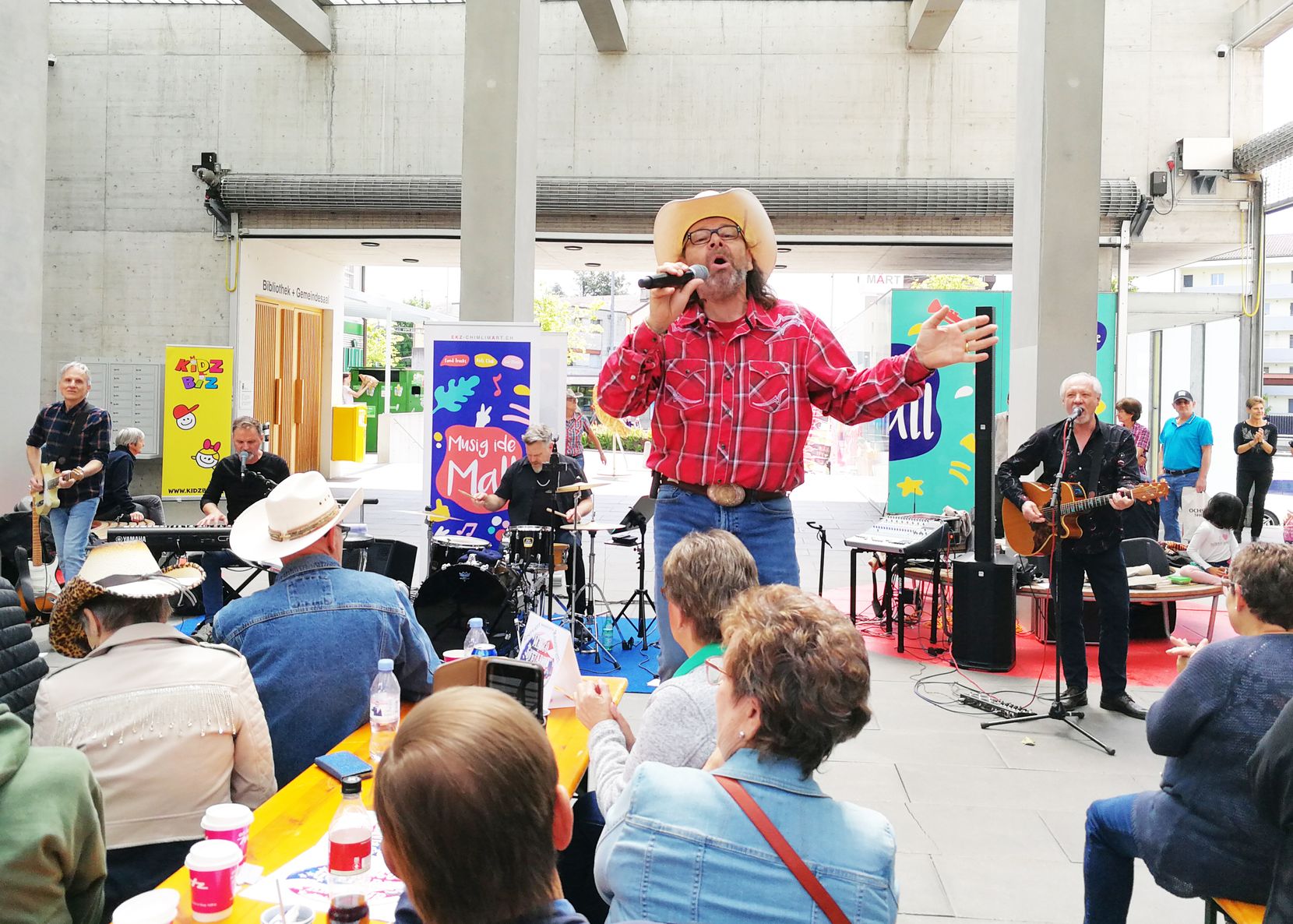 Viele Menschen sitzen auf Festbänken, ein Mann mit Cowboyhut steht dazwischen und singt.